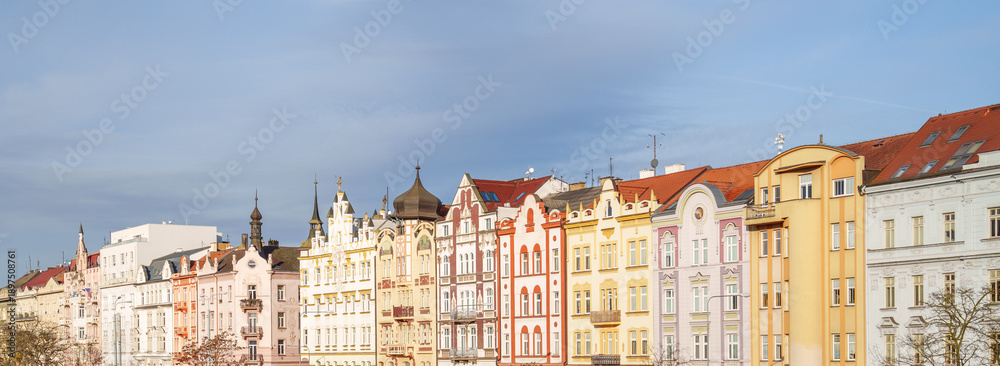 Fototapeta premium A row of colorful buildings with a cloudy sky in the background in Pilsen city in Czech Republic. The buildings are tall and have many windows