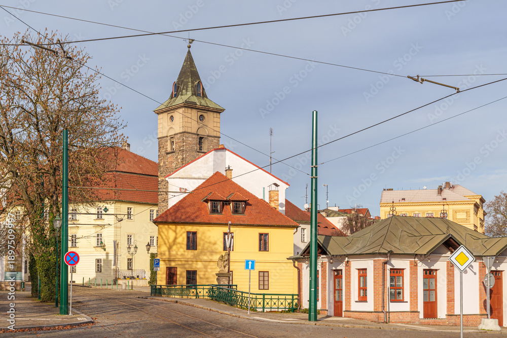 Obraz premium A small town with a yellow building and a red roof in city Pilsen in Czech Republic. The buildings are old and the street is lined with trees