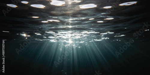 Beautiful sunbeams shine through the dark rippling water surface into the ocean depths