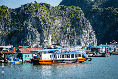 Touristenboot im schwimmenden Dorf vor Karstfelsen in Vietnam