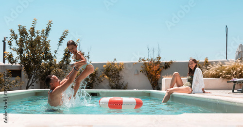 Family enjoying summer vacation splashing in swimming pool