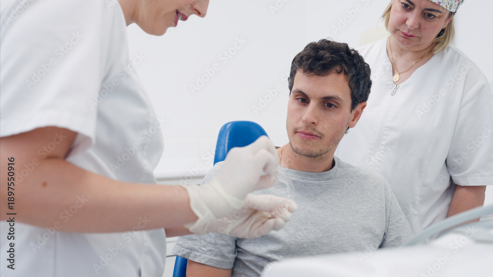 Obraz premium Dentist in protective gloves explaining clear aligner treatment to a young male patient in a dental clinic