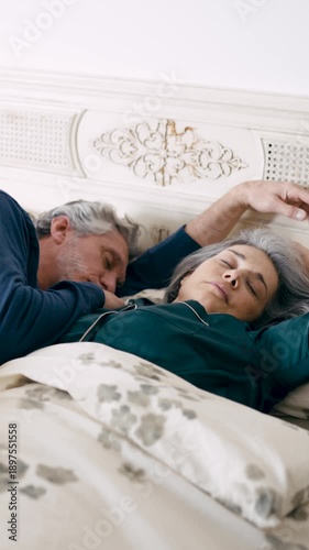 Senior husband and wife resting together in their bedroom. Calm and peaceful partners enjoying a good night's sleep in cozy pajamas. Vertical
