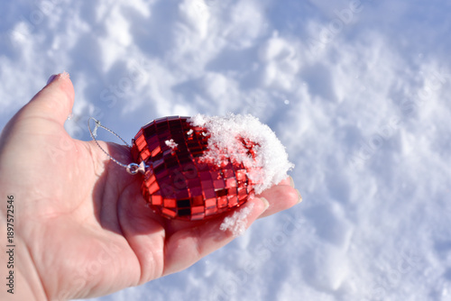Close-up hand holding artificial heart in snow on snowy background,St.Valentines Day backround