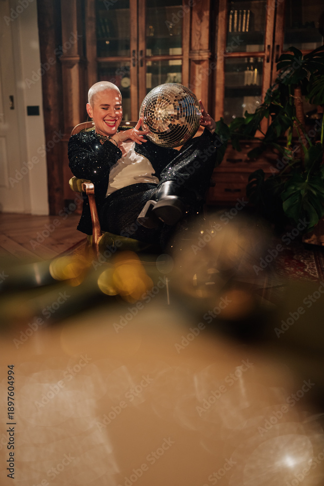 Obraz premium Bald woman celebrating a festive party, holding a sparkling disco ball and laughing in a glamorous outfit