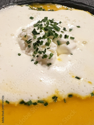 Close up of yellow soup in bowl with cream and seasonings, 