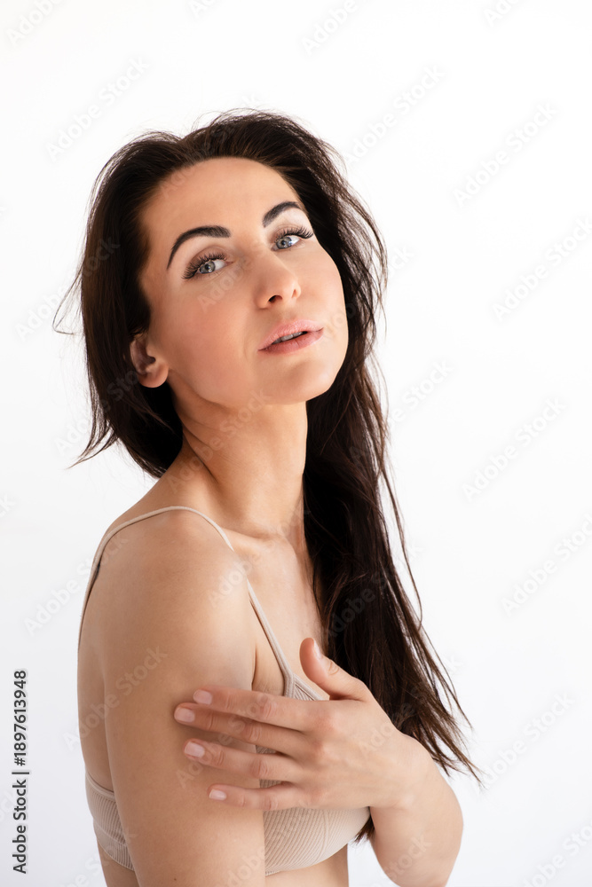 Obraz premium Portrait of beautiful 40-year-old young caucasian woman in sports top. A slender girl touches her shoulder with her fingers, side view. Vertical. Concept of skin care use of sunscreen. languid gaze.