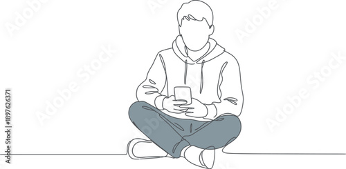 A young man sits cross-legged on the floor, holding a smartphone in a relaxed pose.