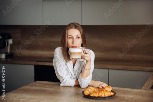 Photos Woman enjoys coffee and pastries in a modern kitchen during a morning routine at