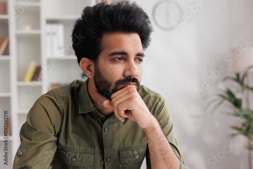 Bored millennial generation man sitting on sofa, feeling lonely at home. Unhappy young male suffering from negative thoughts, having depressive mood or problems in relations, regretting mistakes.