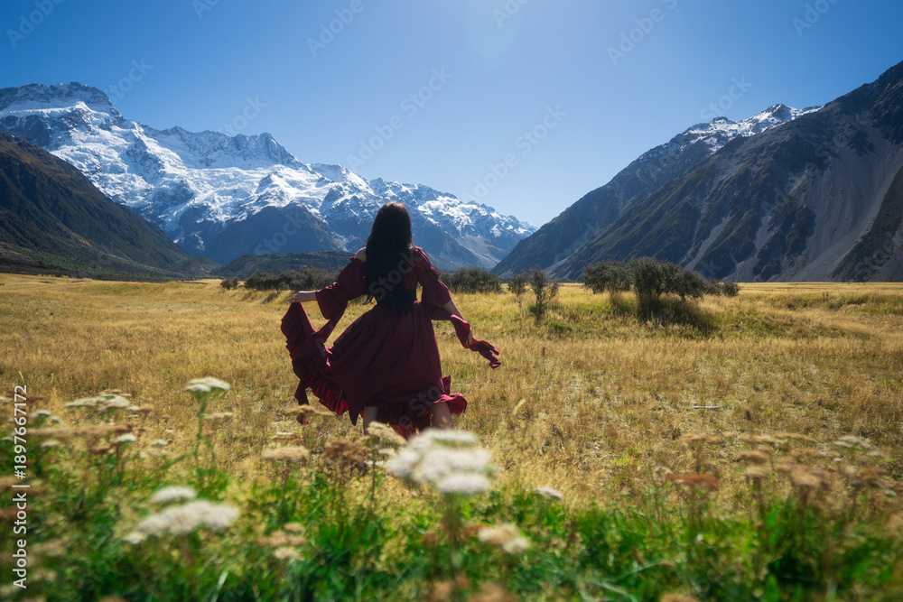 Fototapeta premium Woman in field overlooking alps in long dress