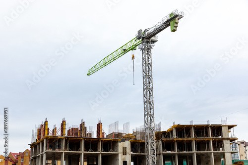 Obraz na plátně Construction site featuring a tall crane lifting materials with a partially completed building and cloudy sky in the background
