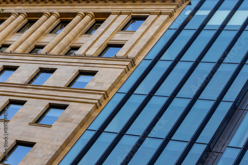 Foto Close-up diagonal composition of heritage sandstone building meeting sleek modern glass facade, contrasting warm masonry details with cool reflective panels in urban cityscape
