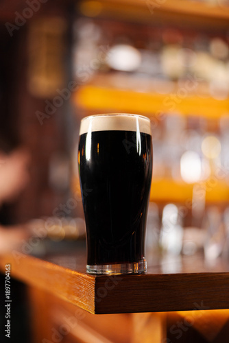Fotografia Dark stout beer served in a glass at the bar
Classic dark beer with creamy foam