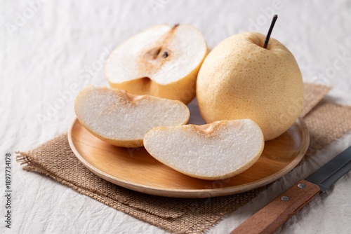 Juicy sliced honey pear on a wooden plate with a paring knife on white fabric background