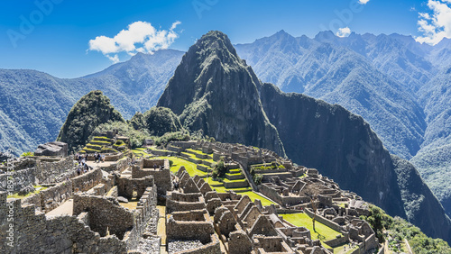 Panorama of ancient Machu Picchu. There are green terraces on the mountainside, ruins of stone buildings, stairs. Masonry walls, empty windows, no roofs. Huayna Picchu, the mountains, the blue sky 