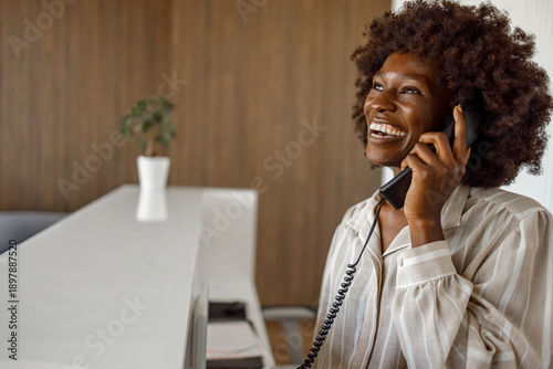 Tableau sur toile Smiling female receptionist talking on phone with guest and making reservation a