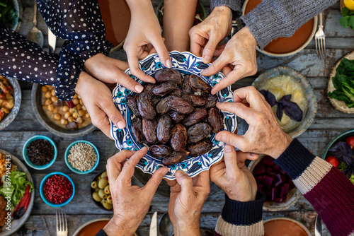 Iftar, break the fasting at holy Ramadan with family, top view of a dining table at iftar time when many human hands sharing their meal. 