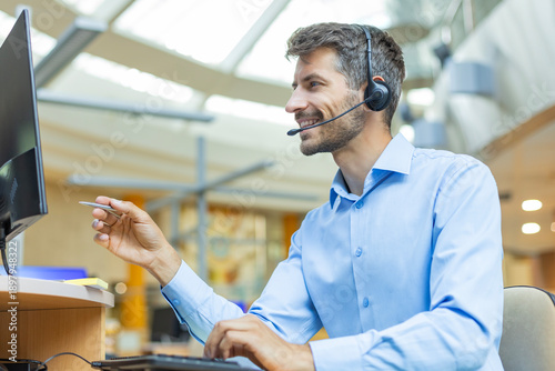 Support service operator talking to customer sitting at desk wearing headset working in modern open space office using PC computer