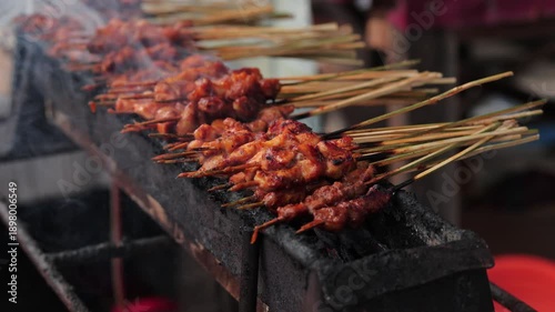 Indonesian chicken satay skewers grilling over hot charcoal with smoke for street food concept