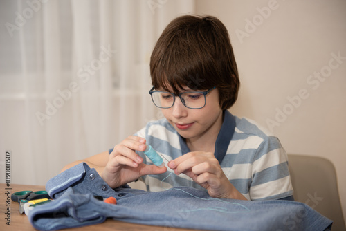 Valokuva Young boy sewing a button on a denim shirt at a home table, focused on stitching and mending the garment