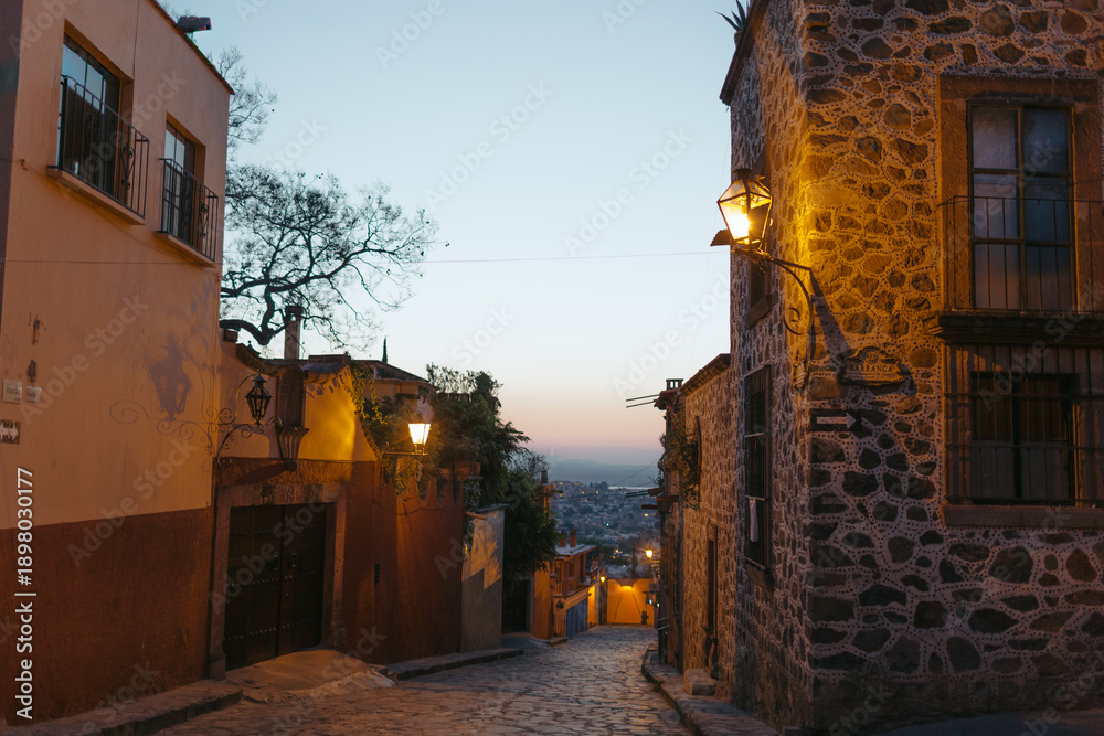 Naklejka premium San miguel de allende cobblestone street at dusk glowing lanterns