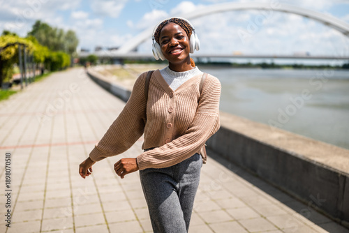 Photos Happy young black woman is walking on foot path, listening music and smiling
