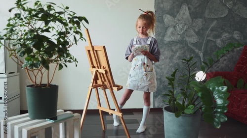 Young artist girl enjoying painting process indoors. Art hobby, imagination growth, creative childhood and artistic expression in cozy home studio environment