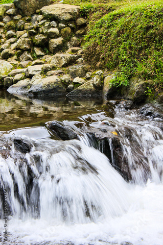 Close Up of Clear River Water Stream Flowing Over Natural Rocks Creating Small Waterfall and White Foam in Tropical Forest Environment for Nature and Freshness Concept