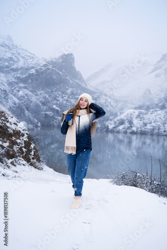 Fotografia A young woman traveler in winter clothes, walking alone outdoors in the snowy mountains, with a thermos, enjoying her winter trip in nature