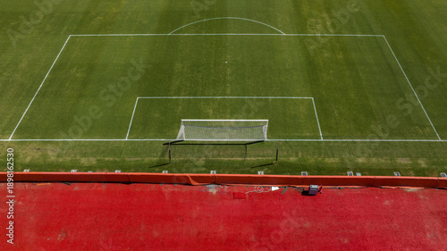 Tablou pe pânză Aerial symmetrical view of a football penalty area and goal on a vibrant green grass pitch, showing clear white boundary lines and the goal net from an elevated perspective
