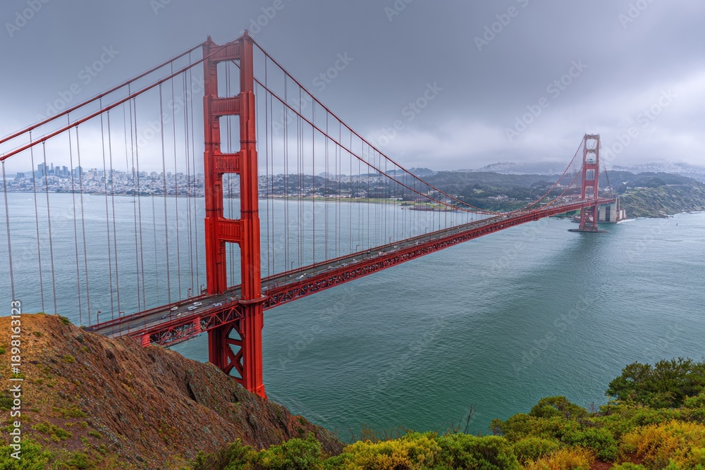 Fototapeta premium Long-span suspension bridge arches over sea to connect land; a rainy, overcast sky above