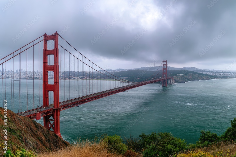 Fototapeta premium Long-span suspension bridge spanning open water under a dramatic, cloudy sky