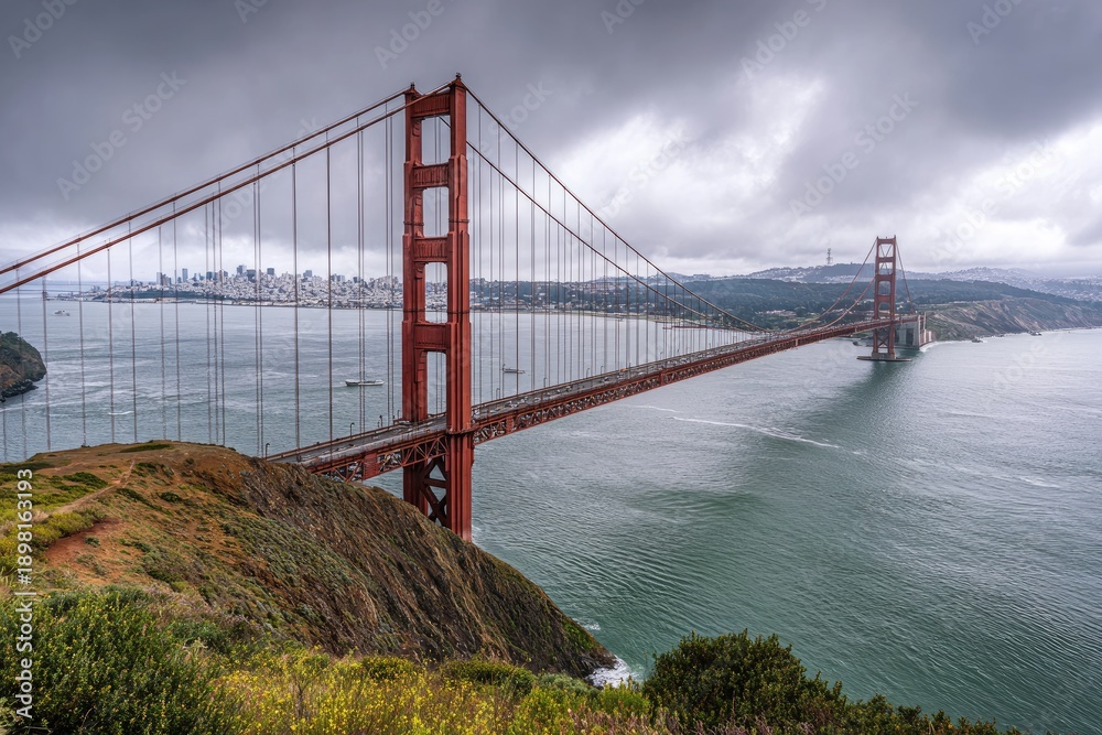Fototapeta premium Famous suspension structure spanning water with a city skyline in background under a cloudy sky