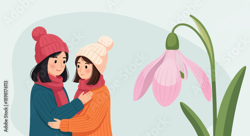 Two girls in winter hats embrace by a delicate pink flower