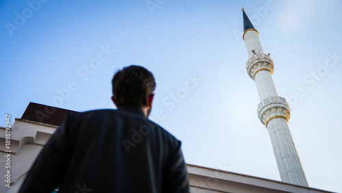 Konstfotografi Young Muslim man looking at a tall mosque minaret under blue sky