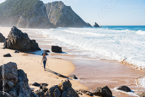 Woman walking along the shore on scenic wild beach. Cabo da Roca, Portugal