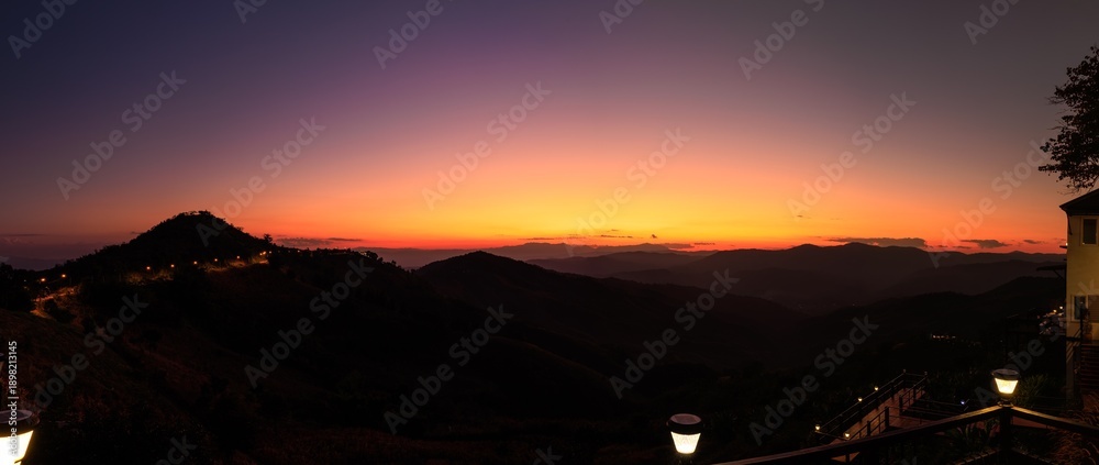 Fototapeta premium Dramatic Mountain Silhouette Landscape During Purple Twilight With Glowing Street Lights And Foreground Lanterns