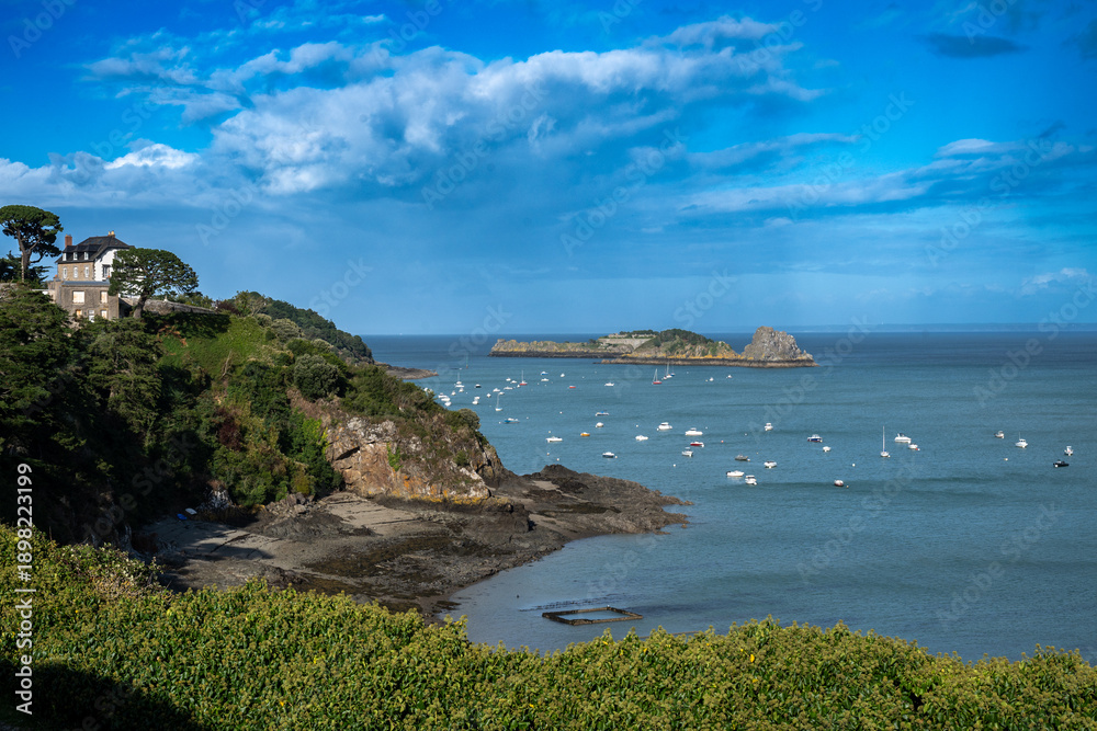 Naklejka premium Cancale à marée basse, montrant les maisons alignées le long du port, le rivage découvert et quelques petites embarcations dans l’eau sous un ciel contrasté.