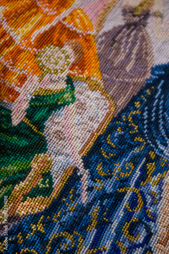 Vertical close-up photo showing a fragment of cross stitch embroidery in progress. Detailed needlework process on fabric, handmade hobby, cozy DIY craft and slow living creative concept.