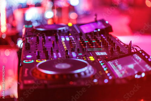 Fotografie A DJ adjusts controls on a professional digital mixer and turntable setup, surro