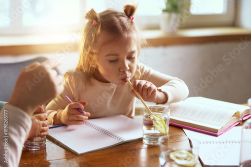 Foto Little girl drinking water with lemon while drawing at table