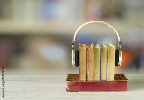 audiobooks concept with  stack of books and headphones on blurry smooth bookshelf background