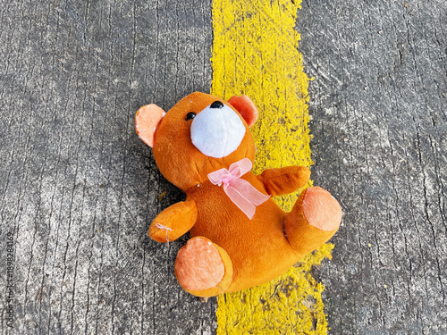 lost small brown toy bear lying on the dangerous yellow traffic dividing line of an asphalt road