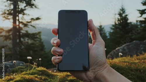 Hand holding smartphone with blank screen in nature landscape with mountains and flowers