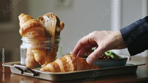 Hand picking green beans from baking tray with croissants and bowl of beans
