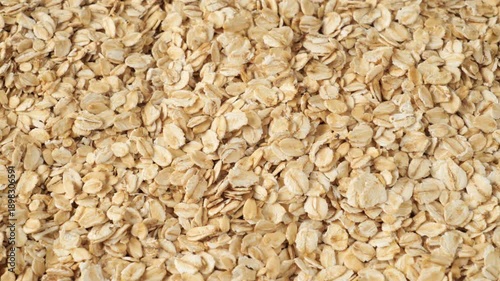 Raw oatmeal flakes pouring down creating a healthy whole grain food background texture.