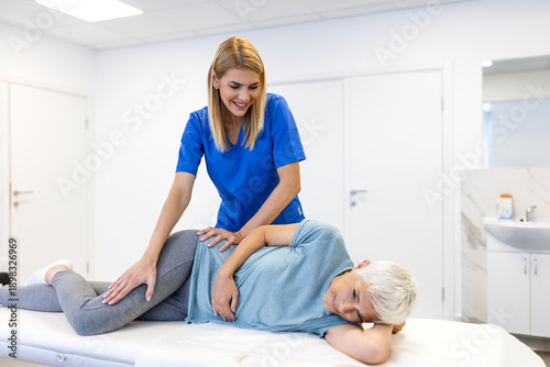 Tableau sur toile Smiling female therapist performing a hip stretch on a senior woman lying on a treatment table