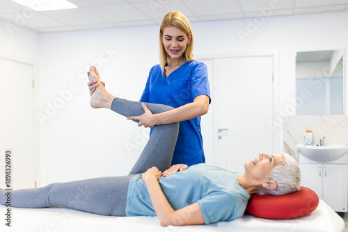 Fotografi Smiling senior woman performing leg stretching exercises with a female physical therapist in a clinic