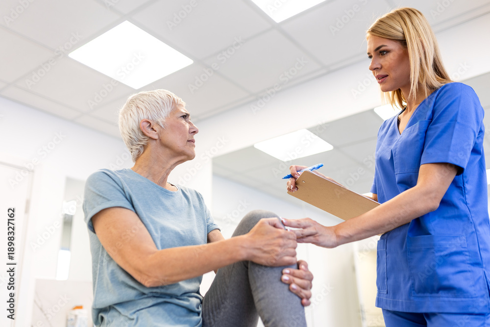 Obraz premium Knee pain consultation. Female doctor with clipboard examining senior woman's knee in clinic. Healthcare and medicine concept, elderly patient discussing joint problems with medical professional.